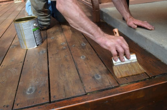 Man backbrushing wood stain into a deck on the outside of a home in Omaha.