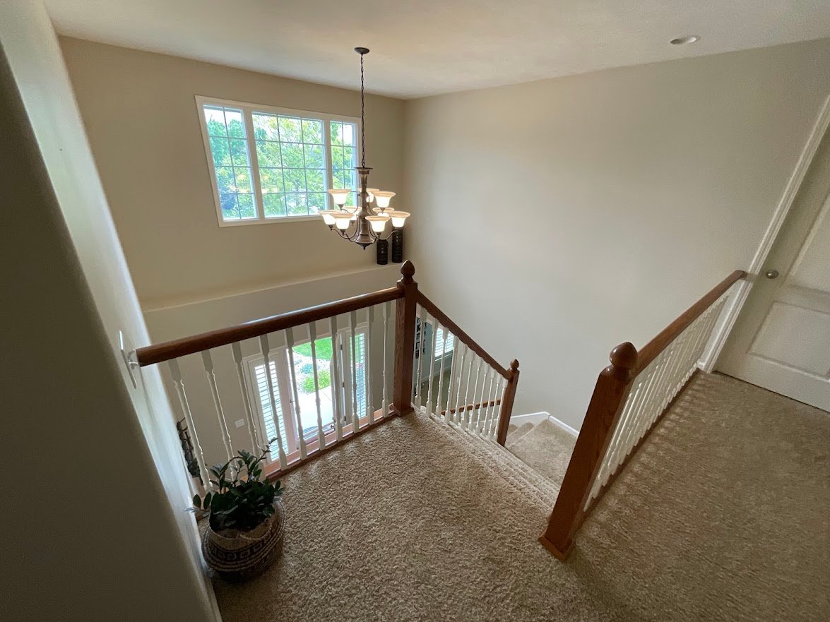 Large entryway before painting with a staircase stained a dark brown with white rods.