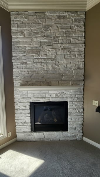 Close up of stone fireplace painted white with a electric fireplace and a shelf.