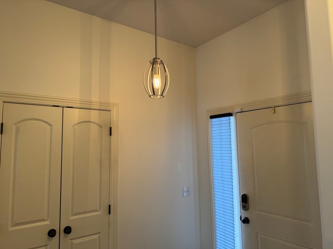 Entryway with a hanging pendant light in the center and the walls painted white with creamy off white closet and main doors and trim.