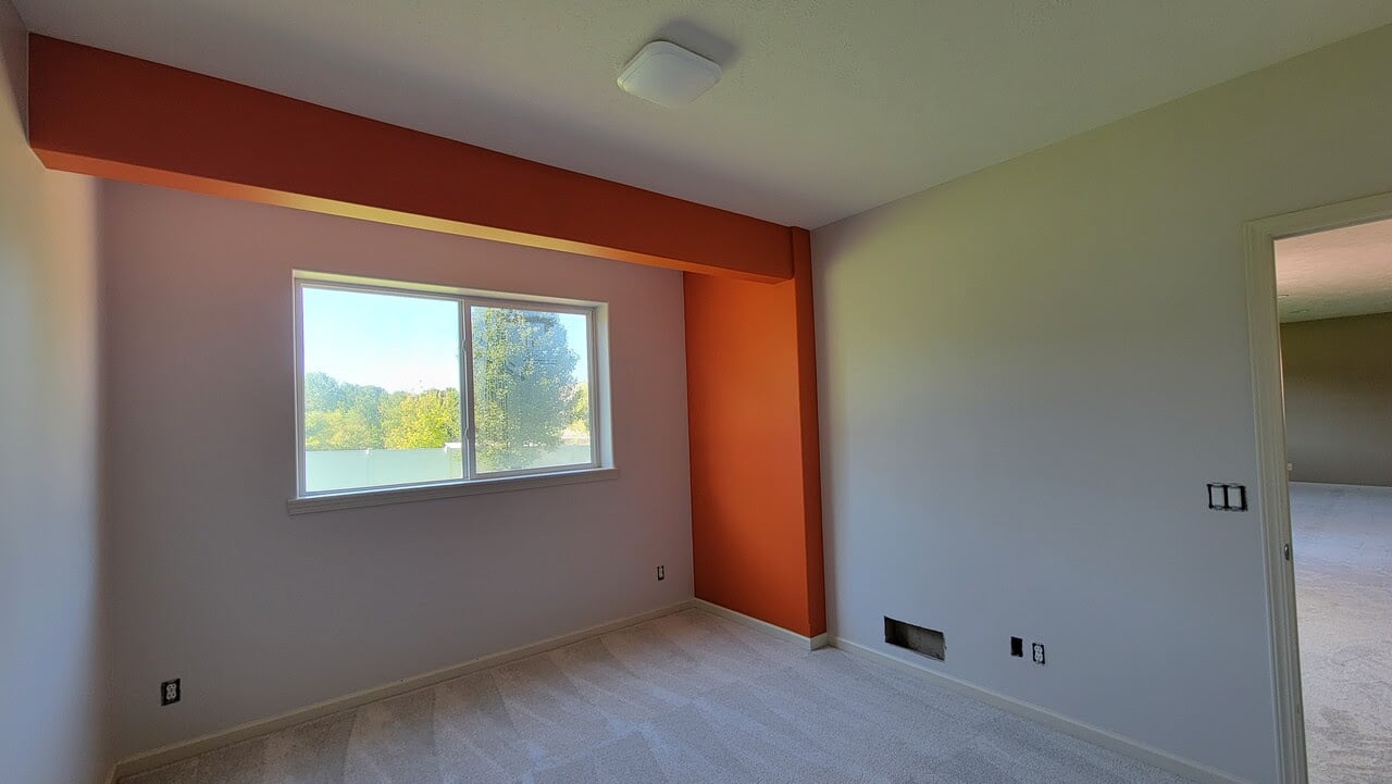 Room with white painted walls with one orange painted section to highlight the room.