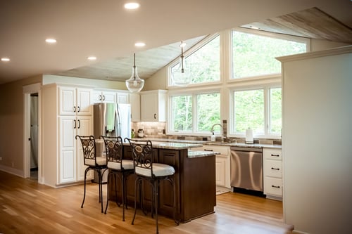 Medium sized kitchen and a large window with white walls and white cabinets and a darker kitchen island.