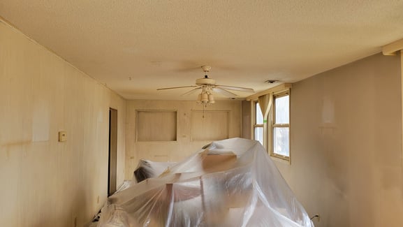 Yellowed room before painting with plastic covering furniture.