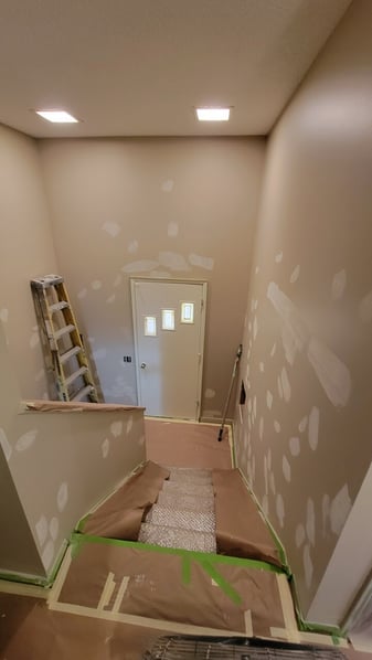 Stairwell and entryway in a home in the process of being painted with spackle and primer covering holes on the walls.