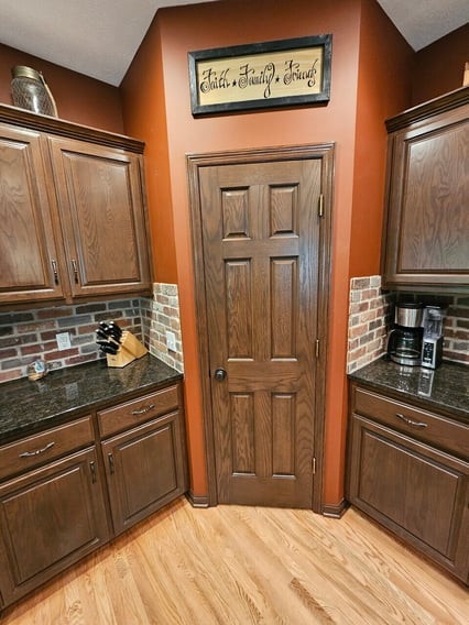 Kitchen cabinets and pantry door and woodwork stained and toned a dark brown color.
