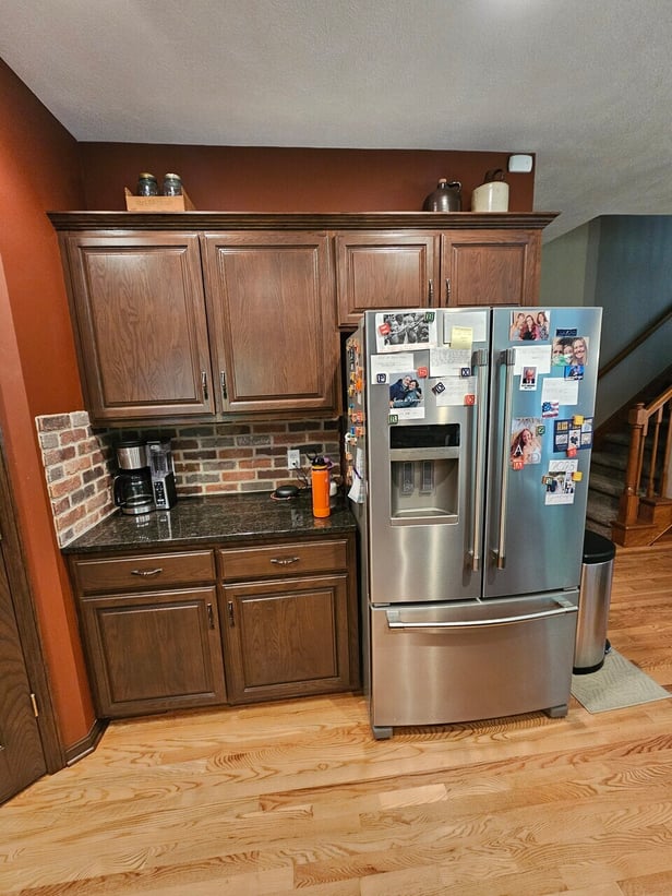 Stained cabinets in a dark brown espresso color with black countertops and a stainless steel fridge.