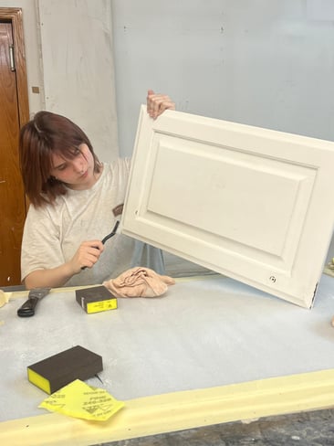 Painter using a brush to clean outside of white cabinet door before painting.