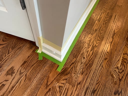 Interior baseboards taped off with painters tape before being painted white.