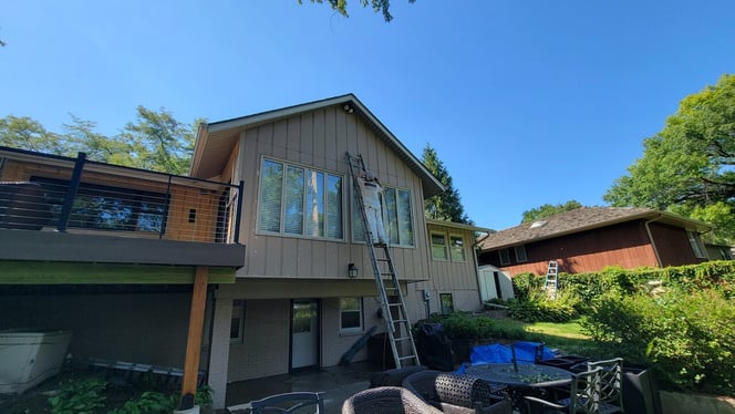 Exterior of house before being painted with a painter on a ladder against the side of the house.