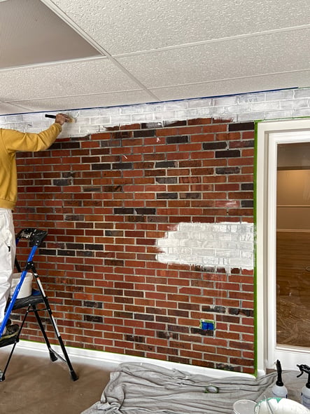 Painter painting brick with white primer before painting.