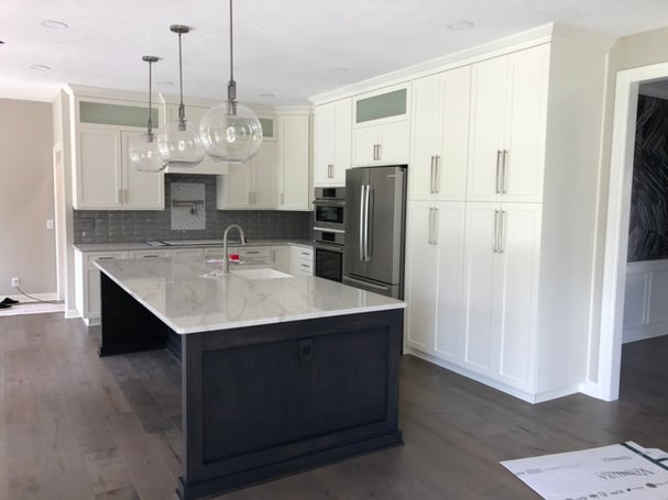 Bright white cabinets in a kitchen with a dark island and marble countertop.