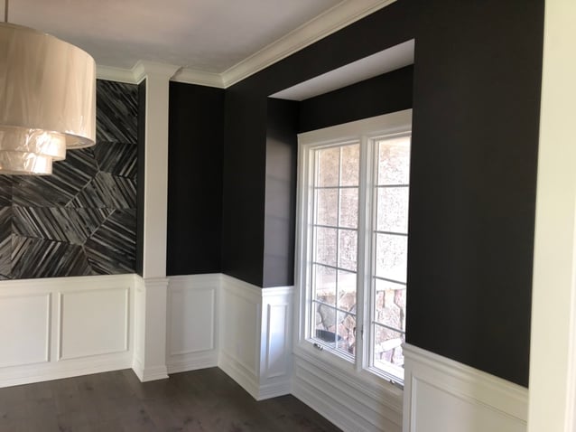 Dining room with walls painted black with white trim and an accent wall with wallpaper.