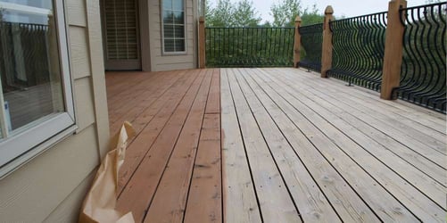 Deck in process of being stained. On the left, the wooden boards are stained a medium brown shade and on the right they are sanded, ready to be stained.