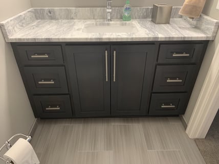 Bathroom vanity painted darker grey/black with a marble countertop and silver handles.