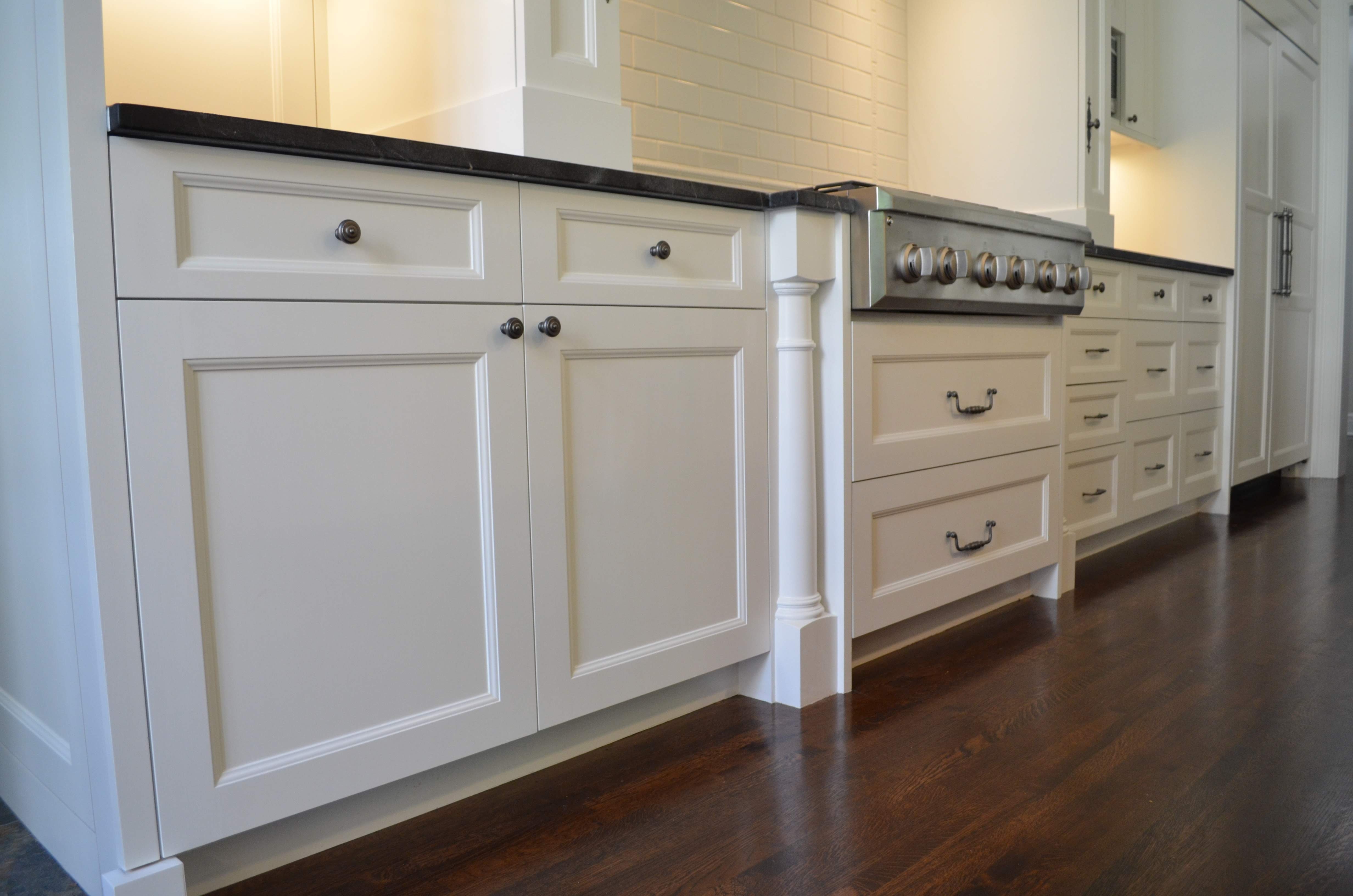 Lower kitchen cabinets freshly painted white with black knobs on drawers and doors.