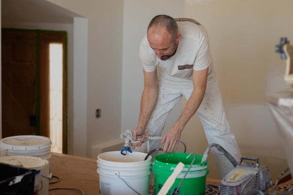 Painter loading a spray gun before interior painting walls and ceilings white.