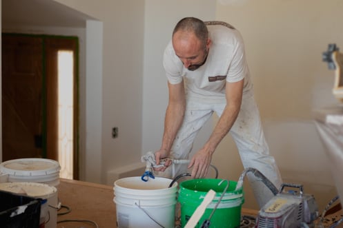 Painter loading paint sprayer machine with paint before painting ceiling inside home.