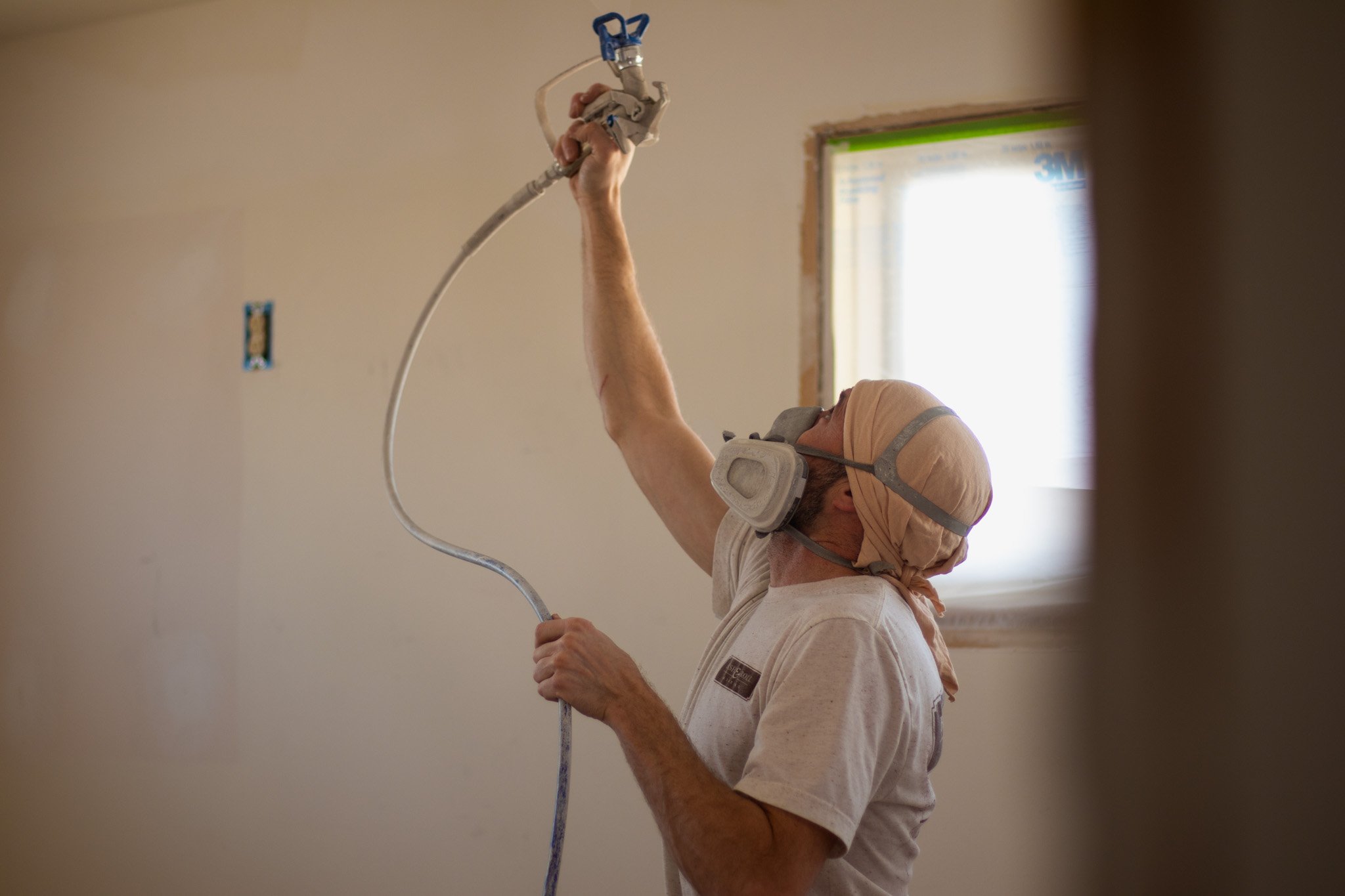 Painter spraying interior ceiling in a home with white paint with a protective mask on in Council Bluffs, Iowa.