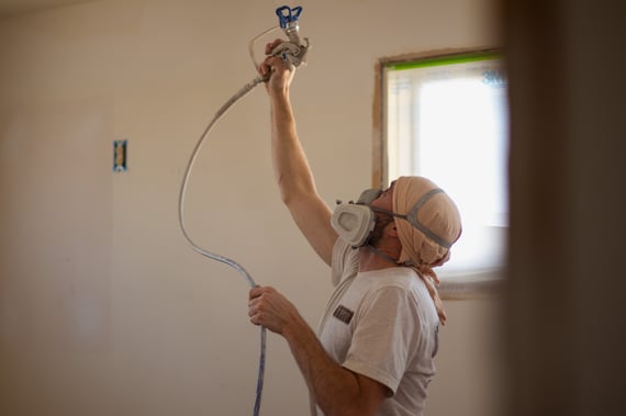 Brush & Roll Painting painter spraying a ceiling with white paint, wearing face mask protection to avoid paint fumes.