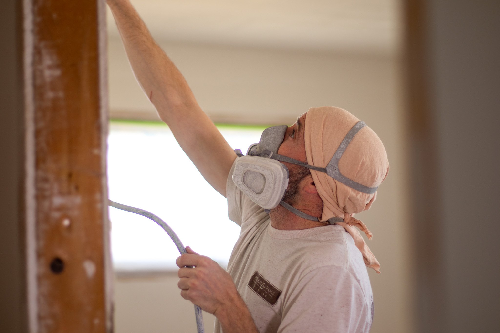 Painter spraying a ceiling with a paint sprayer with protection on their face inside a home in Papillion.
