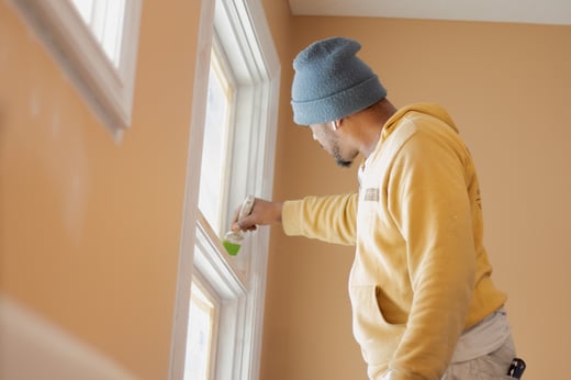 Painter painting interior window sill trim white with a brush.