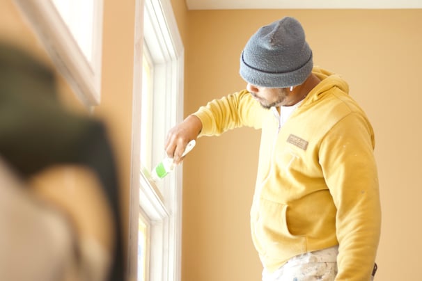 Painter brushing window frames with white paint inside a home in Omaha, NE.