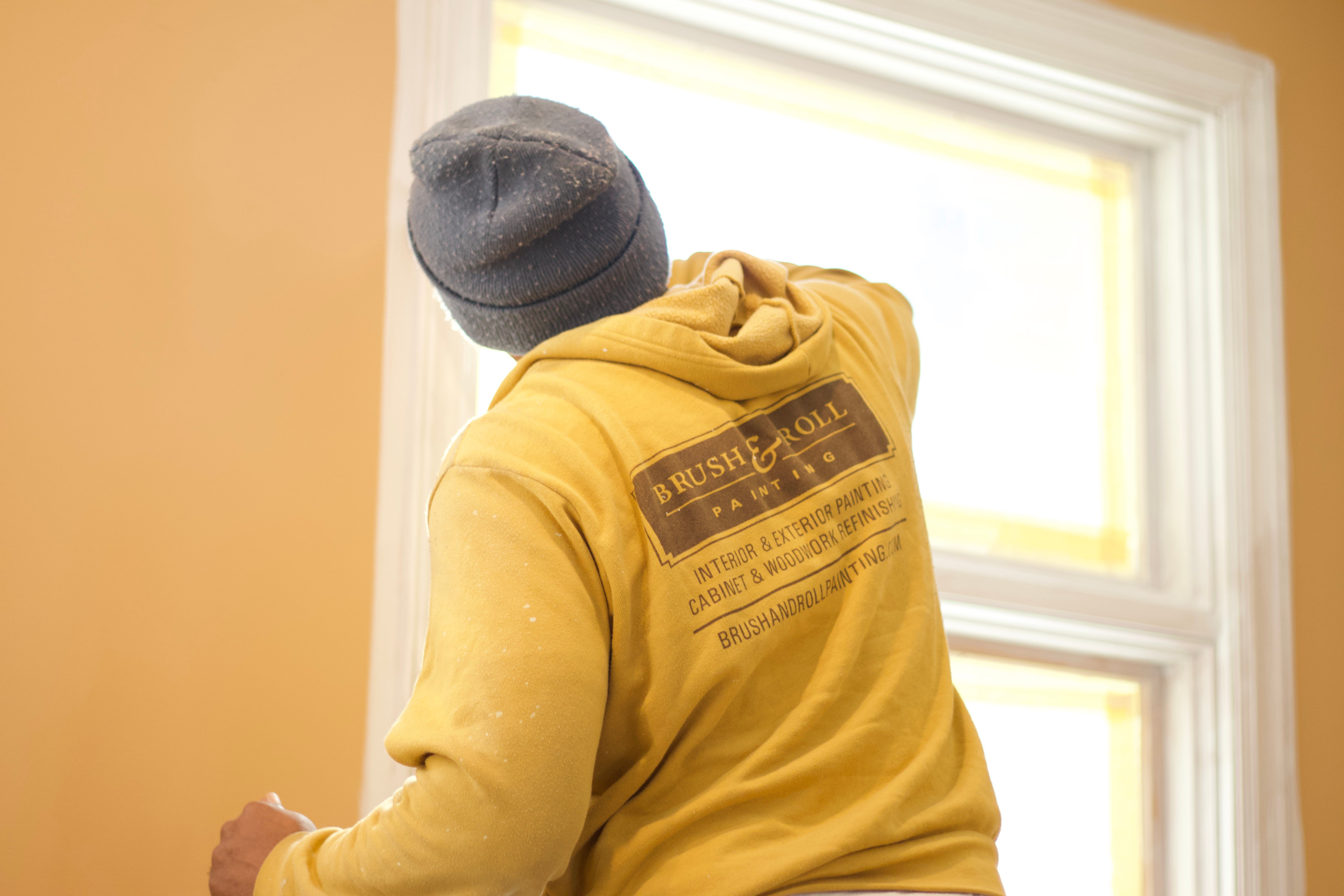 Brush & Roll Painting painter using a brush and woodwork paint to paint window trim white in the inside of a home in Omaha, NE.
