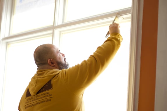 Painter brushing white primer and paint onto interior window frames inside of a home in Omaha, NE.