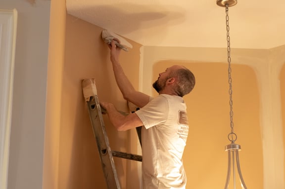 Brush & Roll Painting painter cutting the top of walls next to ceiling with white paint.