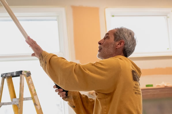 Painter rolling interior walls with paint on a roller.