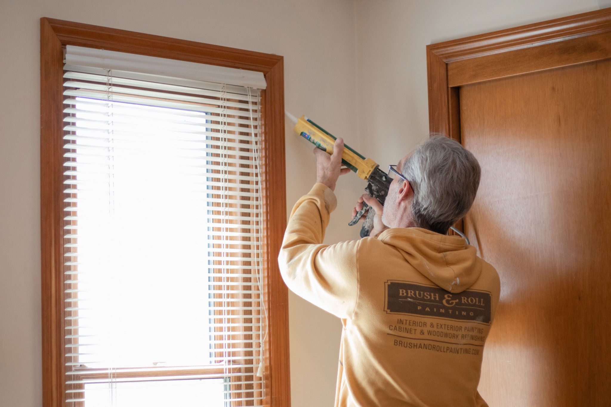 Brush & Roll Painting painter caulking window trim before painting in Omaha, NE.