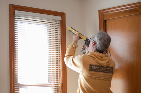 Painter caulking around window trim inside of a bedroom in Omaha, NE.
