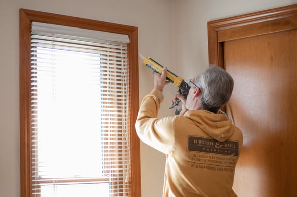 Painter caulking interior window frame with white caulk before painting in Omaha, NE.
