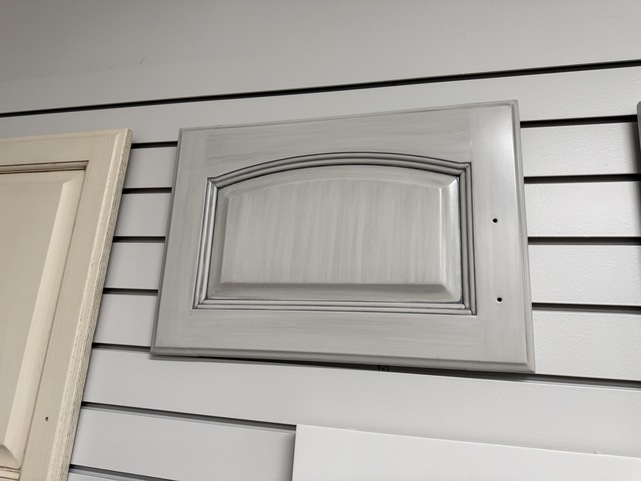Cabinet door sprayed white with a grey glaze brushed overtop of the door to give a detailed and antique look.