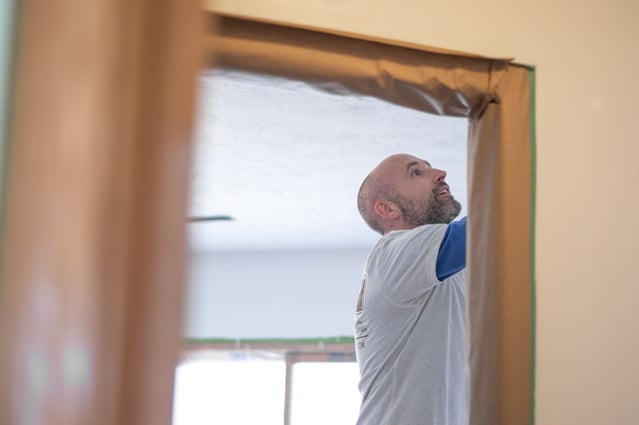 Painter working on interior wall prep in a home before painting over white walls.