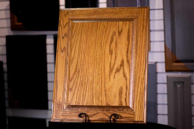 Oak wood cabinet door with a clear coat over most of the surface with the corner showing the original faded wood before painting clear coat.