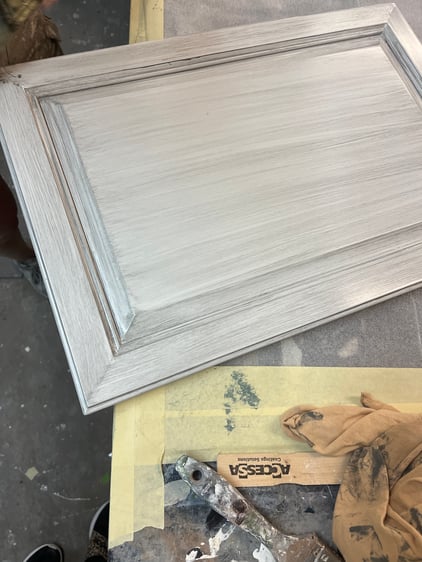 Cabinet door with a light grey glaze on top of a white solid color paint.
