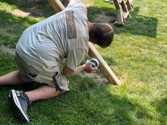 Brush & Roll Painting painter sanding a wood playground set before restaining it.