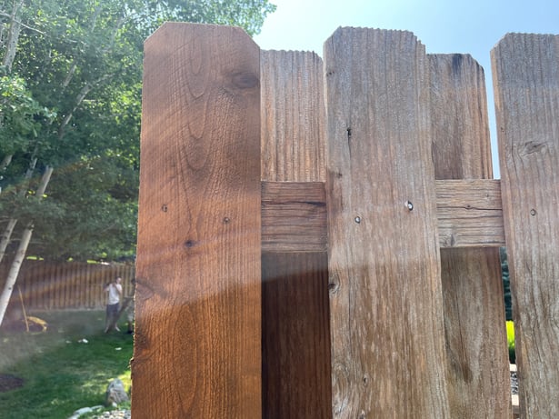 Fence showing before and after staining on a post in a backyard in Omaha, NE.