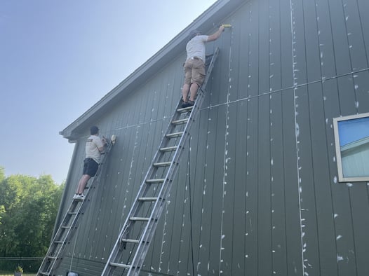 Painters caulking gaps in exterior of house before painting in Omaha, NE.