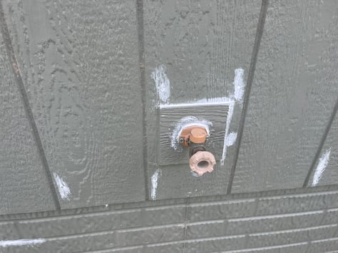 Dark green exterior siding on home and a water hose with caulk around the base.