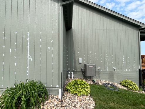 Exterior of home painted sage green with white caulk around gaps and on nail holes