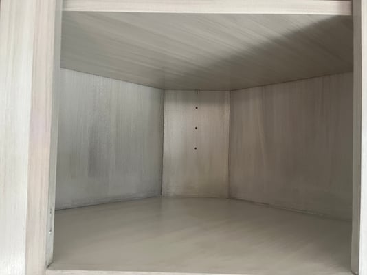Inside of a cabinet box that has been painted white and glazed with a grey glaze with a glass cabinet door on it.