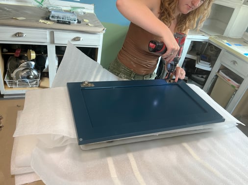 Soft close hinges being installed on cabinet doors freshly painted a navy blue color.