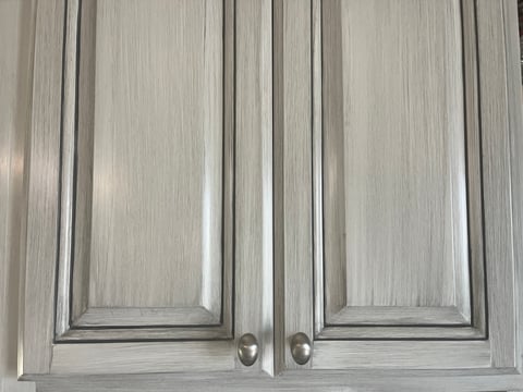 White cabinet doors with a grey glaze and silver knobs.