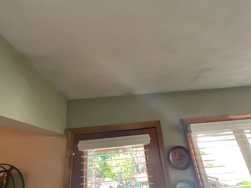 Room with sage green interior wall paint, windows with golden oak trim, and a white ceiling with dark shadowed spots due to poor insulation.
