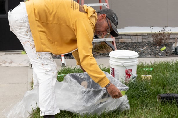 Painter taping paint bin with plastic before filling with paint for exterior of house.