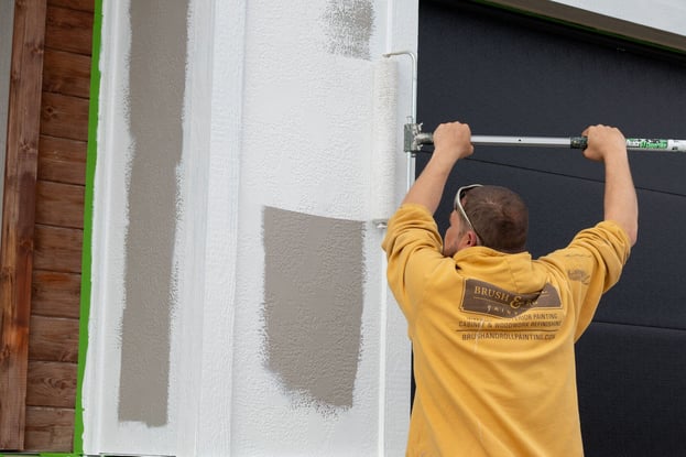 Brush & Roll Painting painter rolling white paint onto exterior edge of house in Omaha.