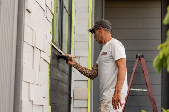 Brush & Roll Painting crew lead brushing black paint on the exterior siding of a house in Omaha, NE.