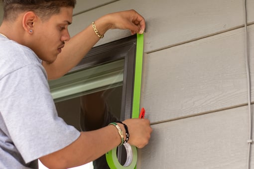 Painter putting up tape on window trim to protect it from paint when exterior painting in Omaha, NE.